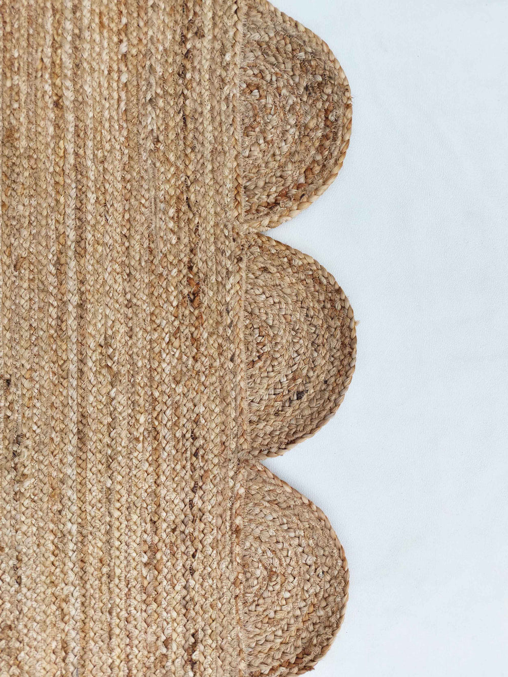Beige braided rug with scalloped edge on a white background