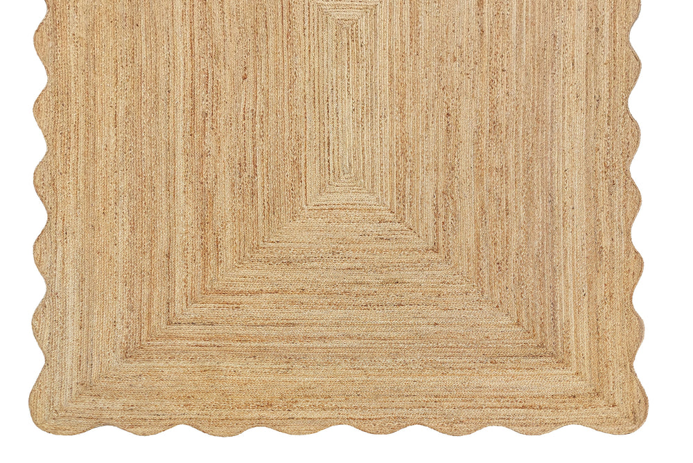 A beige-colored, textured jute area rug with a wave scalloped edge.