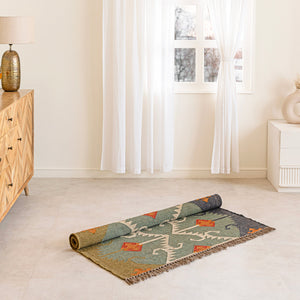 Rolled-up patterned rug on a light wooden floor with a wooden cabinet and lamp in the background.